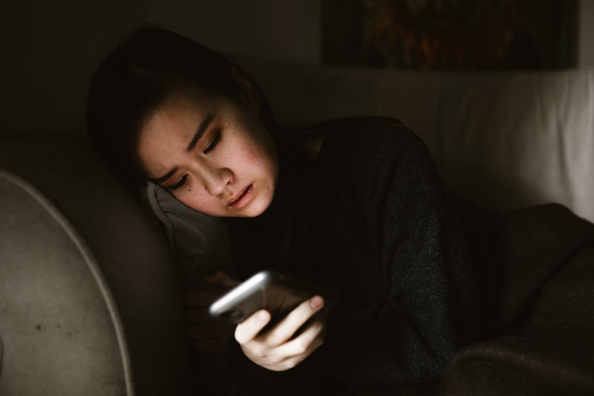 Person lying on a sofa scrolling their phone in dim light